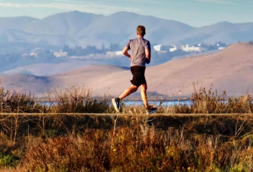 Mann joggt auf Feldweg vor Bergen, Outdoor-Lauftraining in Naturlandschaft