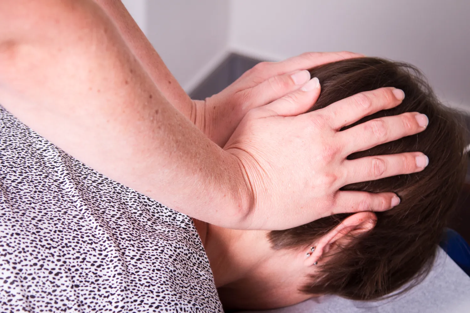 Therapeutin hält Kopf einer Patientin bei Physiotherapie im Nackenbereich